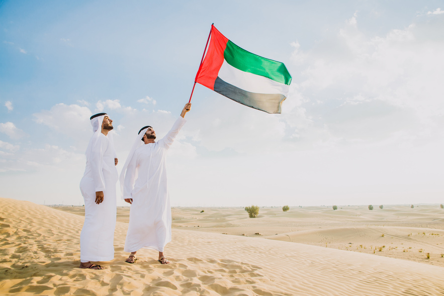 Men Wearing Traditional Kandura Waving UAE Flag in the Desert